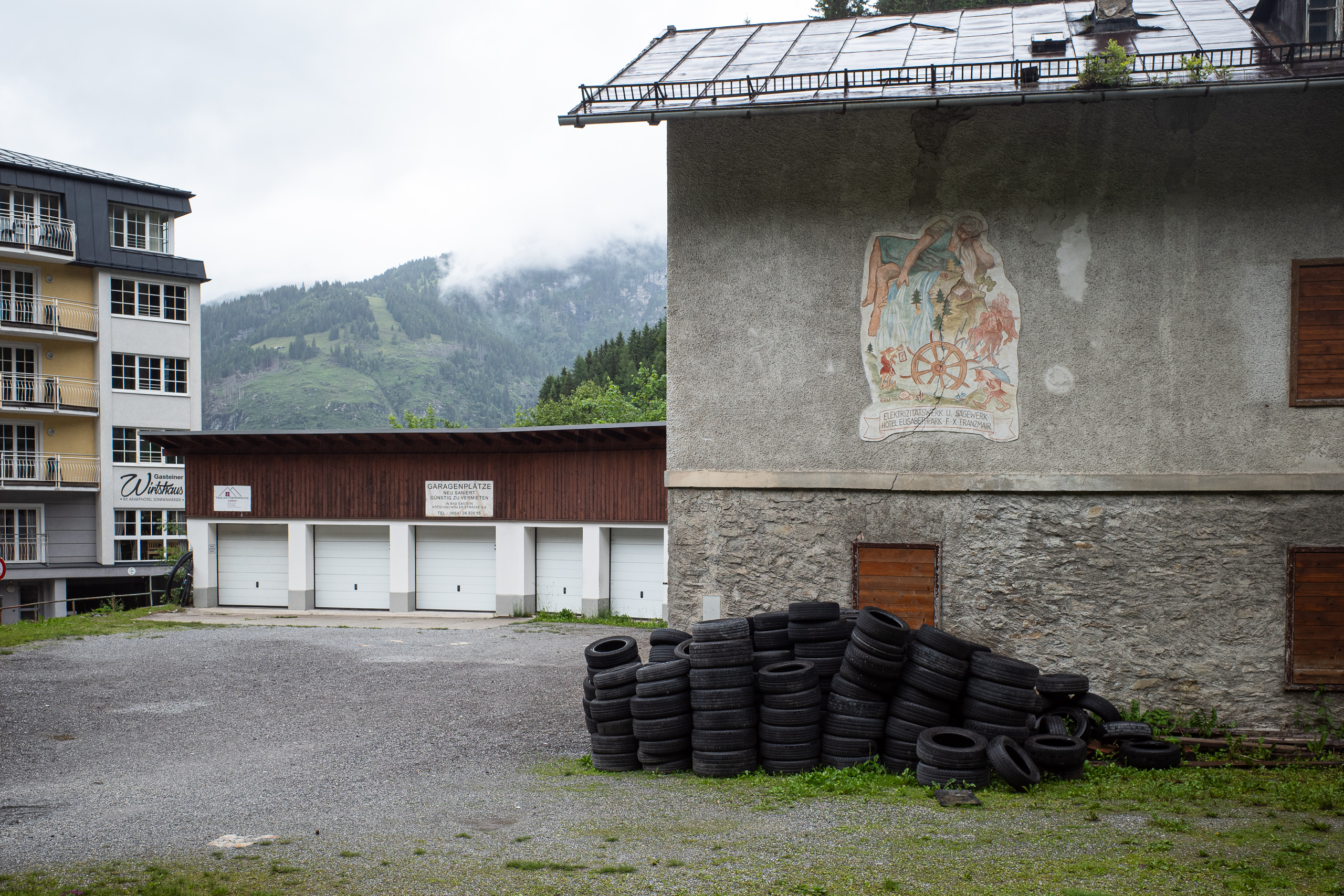 Verblasstes Fresko am alten Elektrizitäts- und Sägewerk, davor ein Berg Altreifen